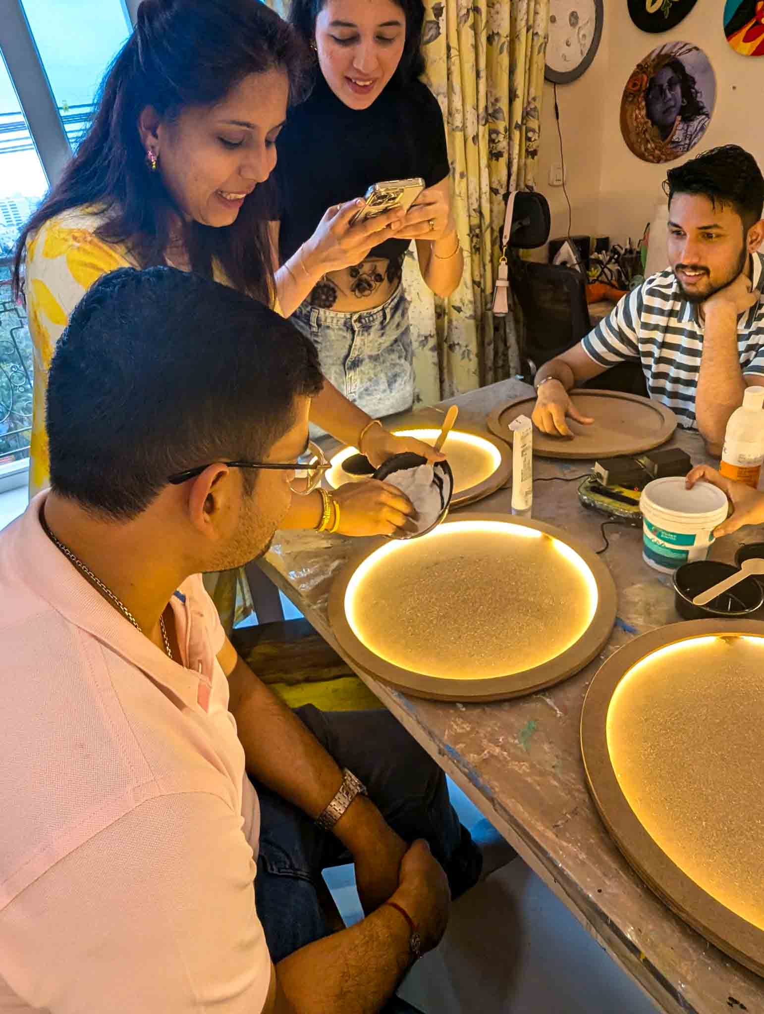 Group of people working together shaping and prepping moon lamps on a table with glowing circular bases.